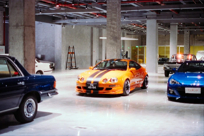 Orange sports car with racing stripes in showroom.